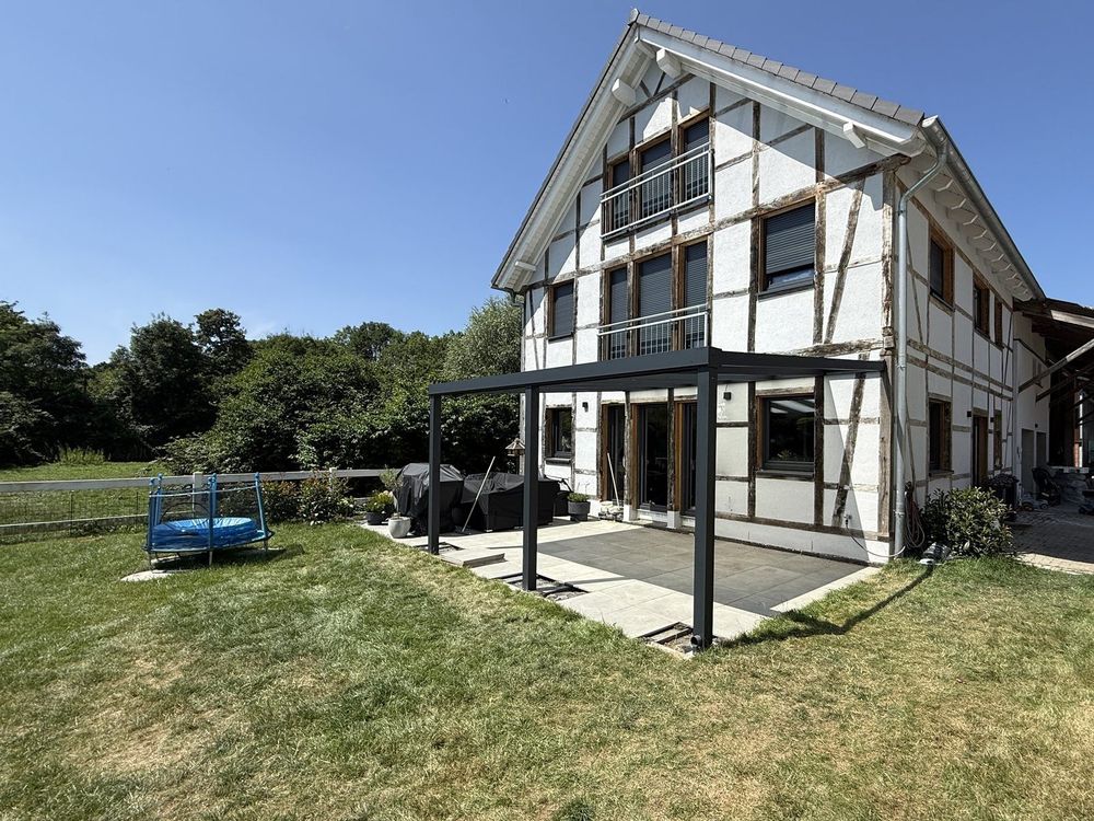Terrassendach mit Glaseindeckung und schlanken Aluminiumpfosten über einer Terrasse mit Rasenfläche