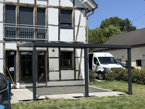 Fertig montierte anthrazitfarbene Terrassenüberdachung an einem Fachwerkhaus mit Garten