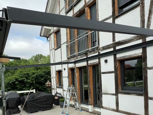 Aluminium-Sparren einer Terrassenüberdachung werden an einem Fachwerkhaus montiert