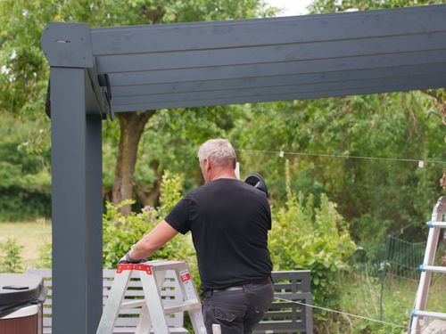 Monteur auf der Leiter unter einer anthrazitfarbenen Terrassenüberdachung aus Aluminium